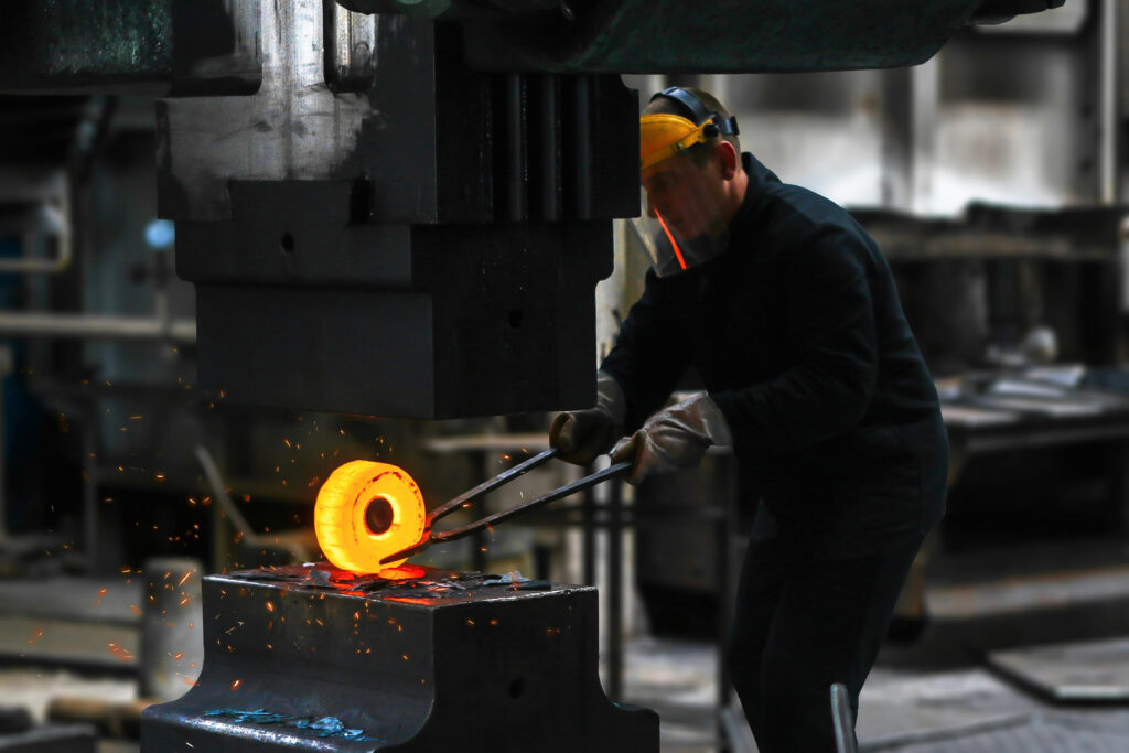 Worker shaping a glowing metal piece, illustrating manual labor and automation fusion in manufacturing industry trends.